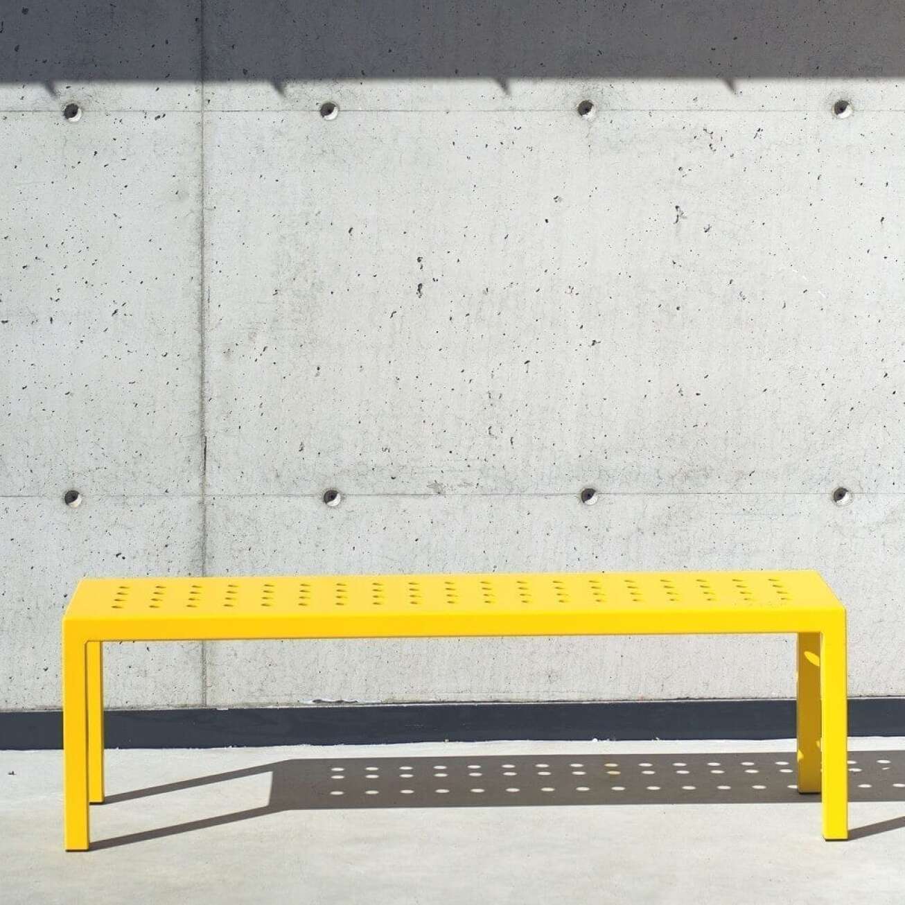 Gul benk ​​foran betongvegg i sollys