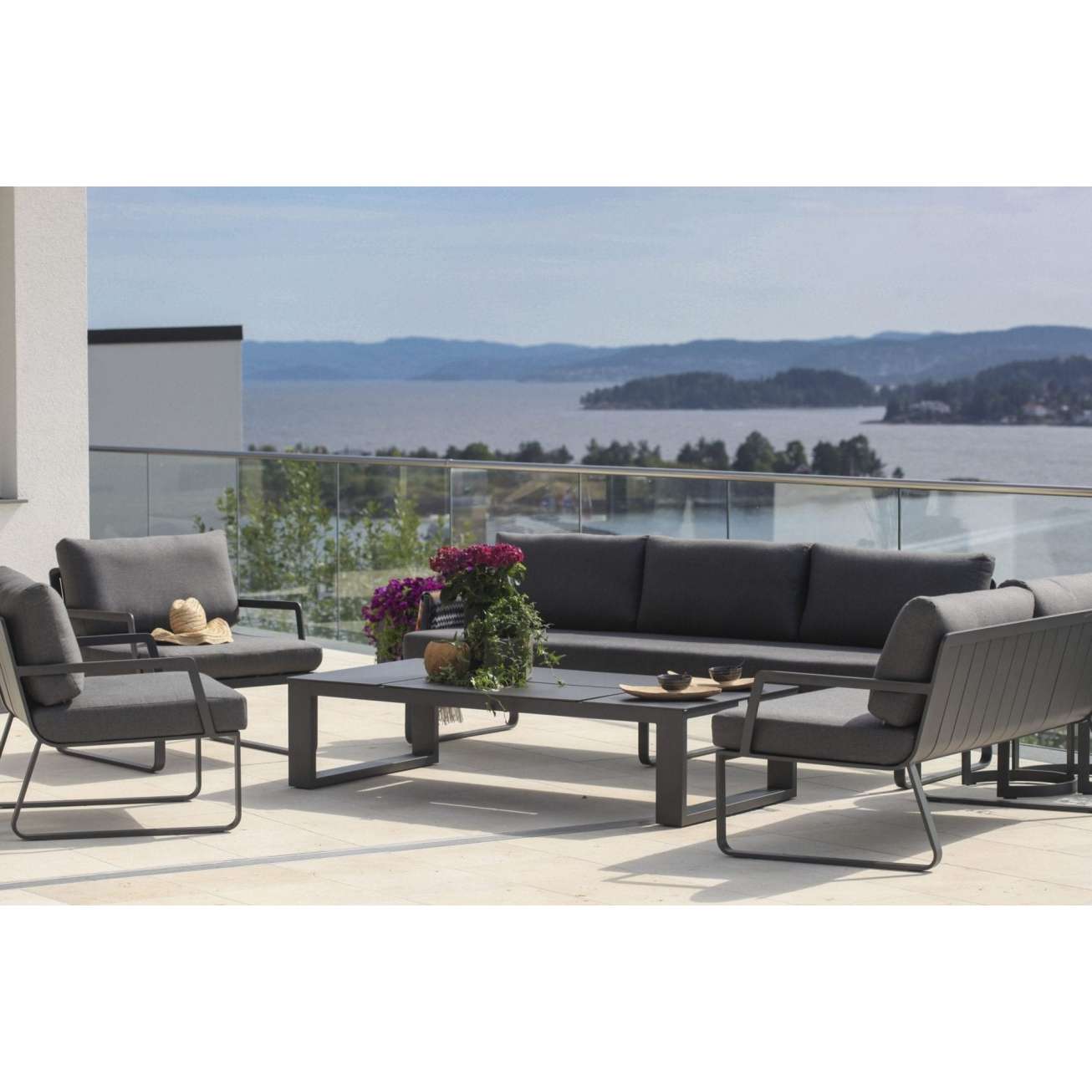 Sofagruppe - 3-seter og tre hagestoler i sort aluminium med grå puter sammen med et hagebord på veranda