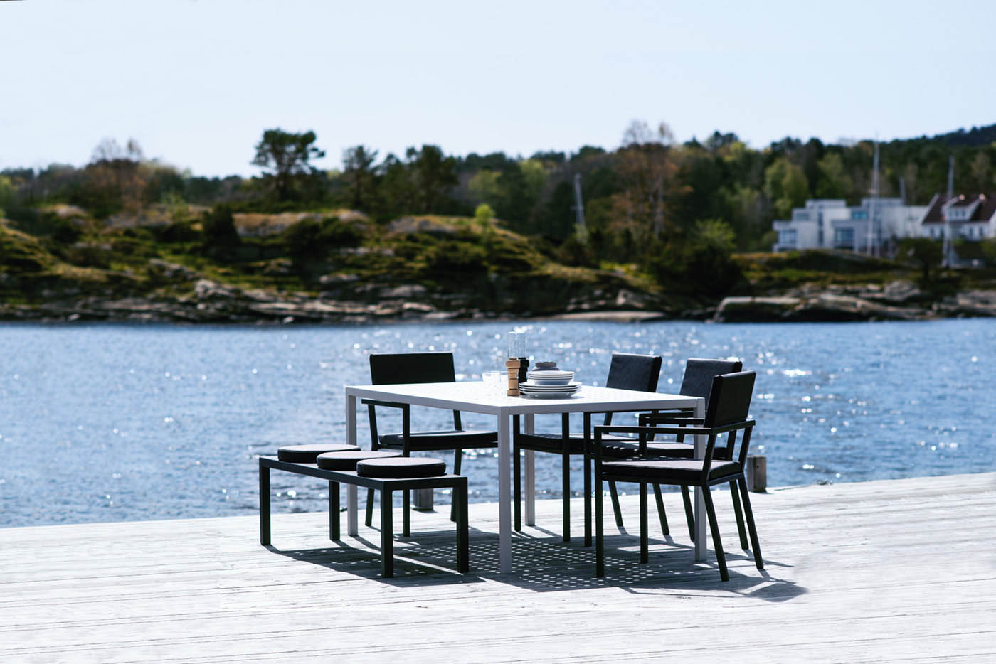 Frame spisebord fra Sundays Design hagemøbler i strålende solskinn med en glitrende sjø i bakgrunnen
