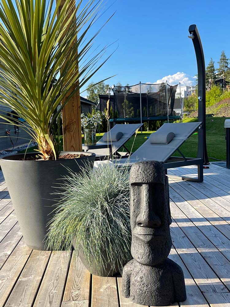 Figur på terrasse ved siden av planter og med solsenger fra Fine Design i bakgrunnen