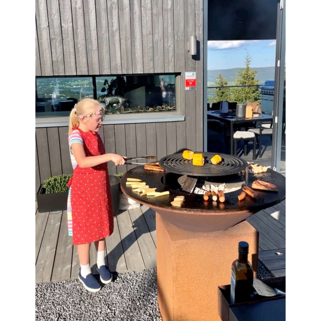Jente griller mat på OFYR vedfyrt grill med lagringsplass på terrasse