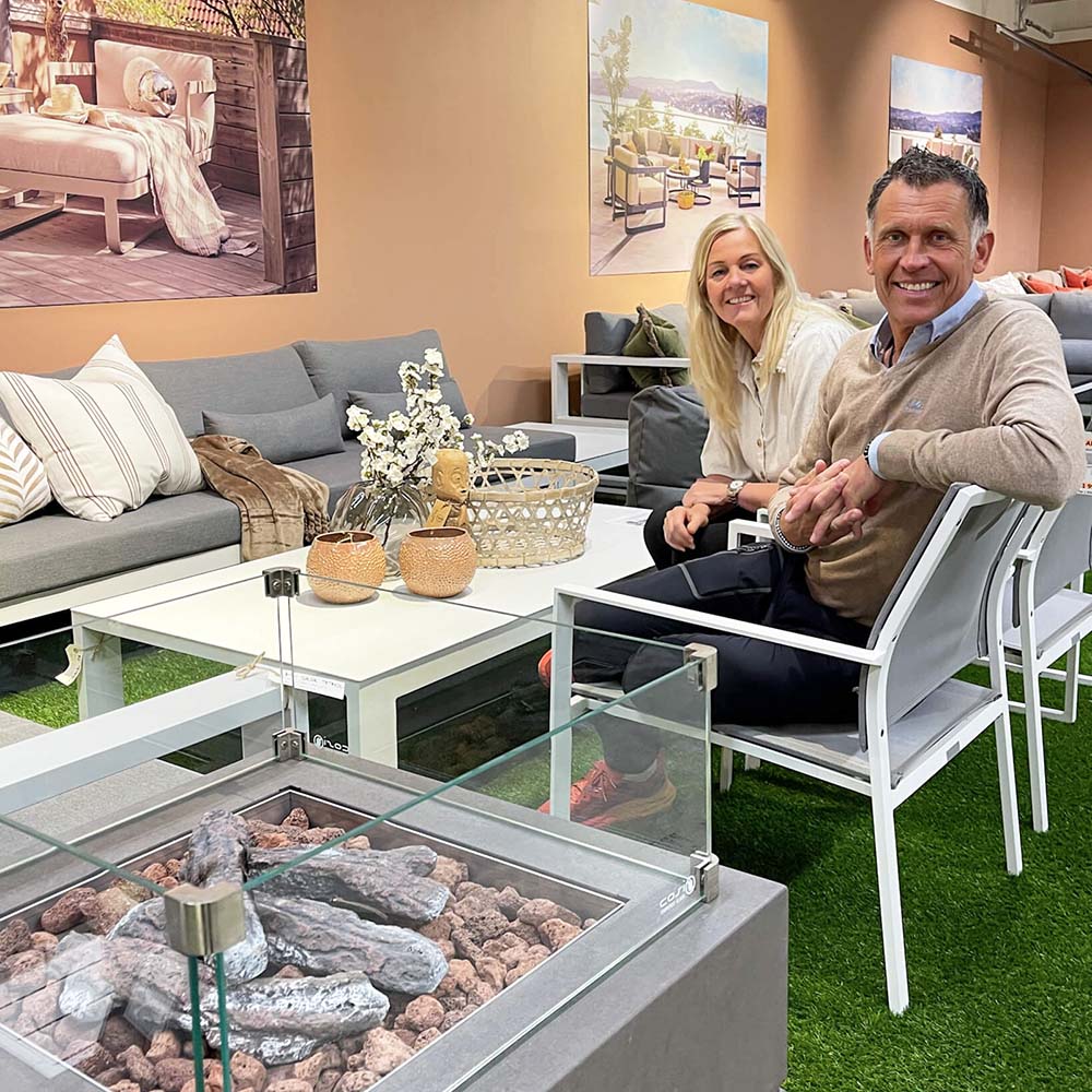Marianne og Kjetil Aanerød i Fine Design hagemøbler i Løxaveien 5 sitter i hagestoler bak gasspeis ved utebord i hvit aluminium